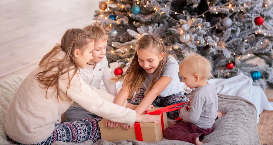 Siblings opening a gift in the family room next to a Christmas tree.